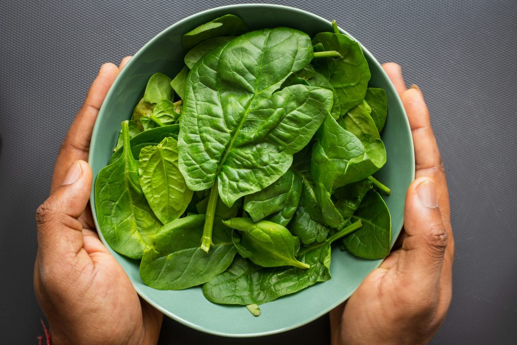 A person holding a bowl of fresh spinach, a natural source of Alpha-Lipoic Acid and essential antioxidants for liver support