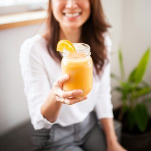 A smiling woman enjoying fresh orange juice, illustrating the energy and vitality gained through working with a Las Vegas Nutritionist