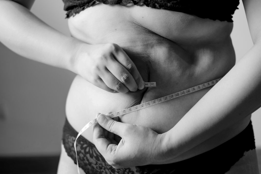 A person measuring their waist with a tape measure, symbolizing the successful results of working with a holistic nutritionist or dietician for weight loss in Las Vegas.